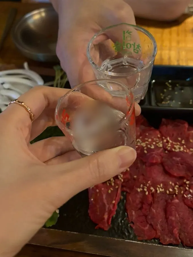 A table with beef sashimi and a glass of soju