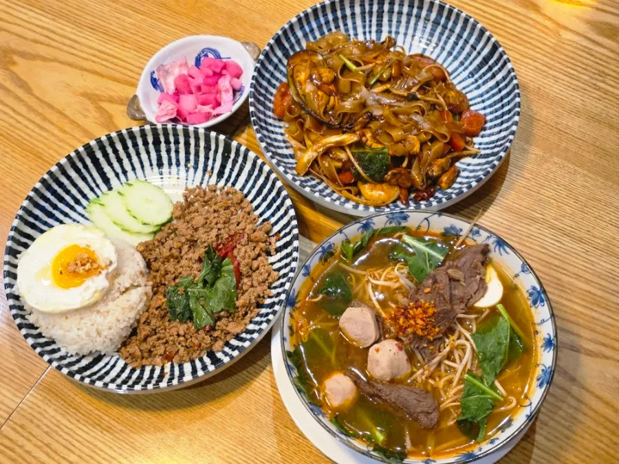Table spread with tom yum rice noodle soup, Thai chili noodles, and basil pork stir-fry