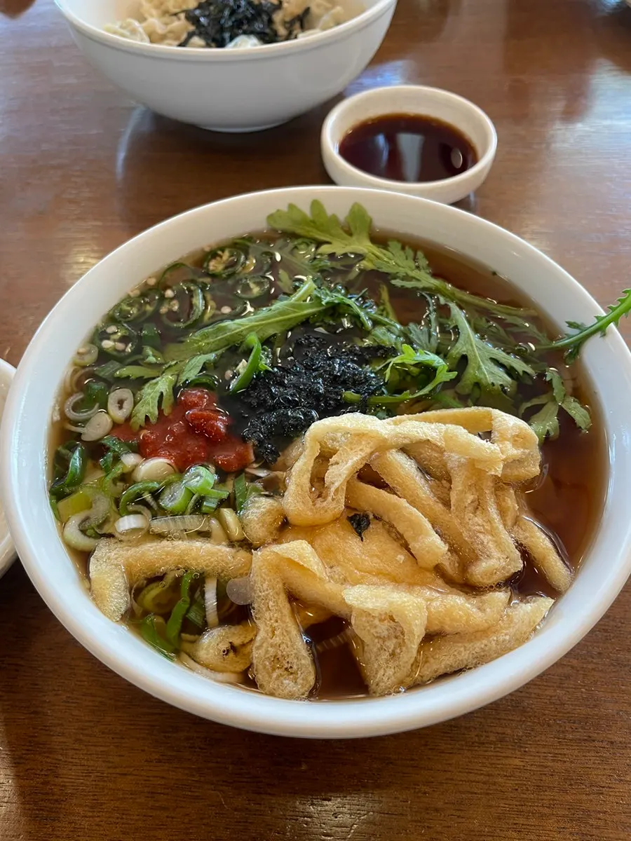Spicy udon, jeyuk deopbap, mandu, and zero-sugar cola all set out together