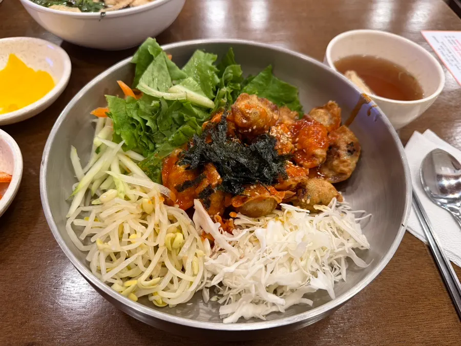 Gakgi udon topped with fried tofu skin, crown daisy greens, and seaweed flakes