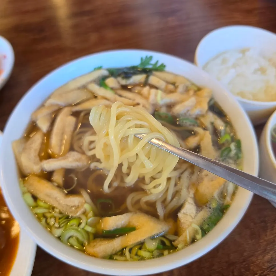 Close-up of gakgi udon topped with scallions, crown daisy greens, and seaweed flakes