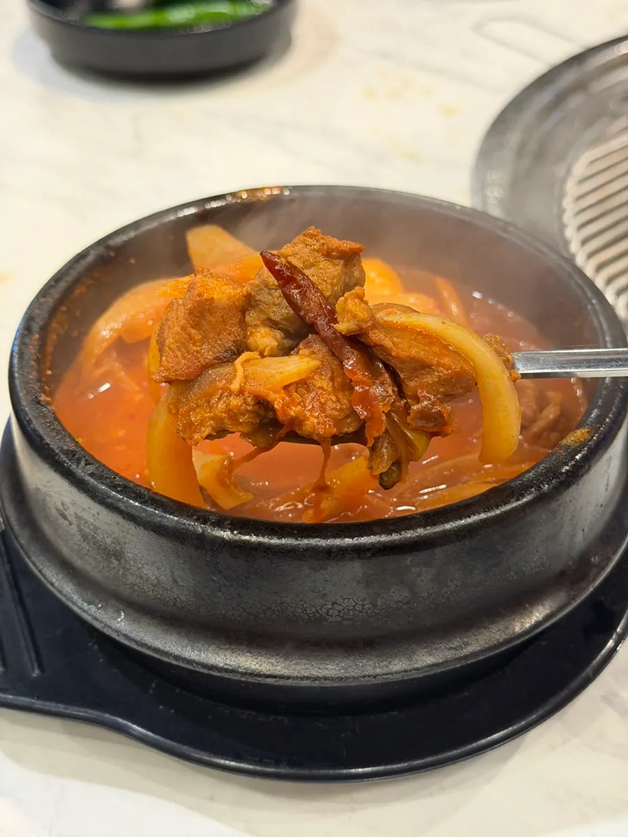Isi jjigae gochujang babi hitam diambil dengan sendok sup