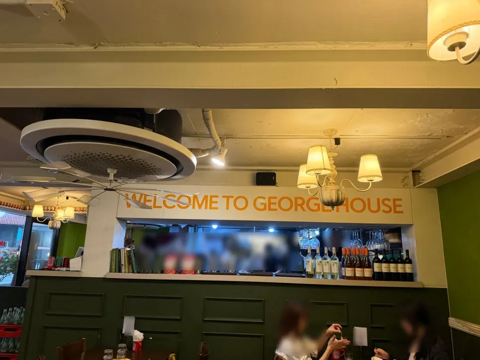 "WELCOME TO GEORGE HOUSE" sign and liquor display above the kitchen bar