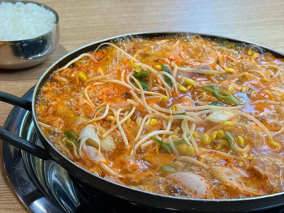 Budae jjigae broth loaded with ham, sausage, and bean sprouts