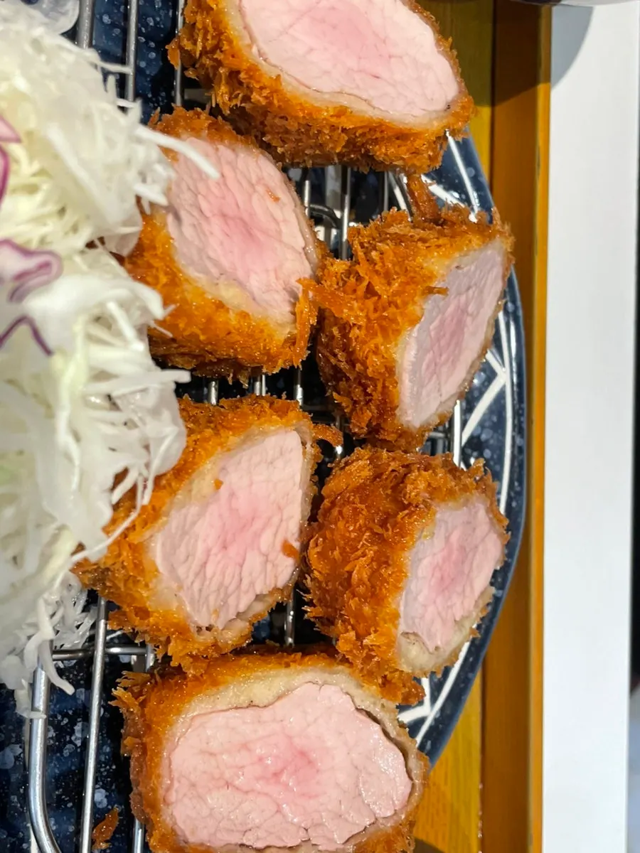 A bite of cheese katsu with wasabi and sauce