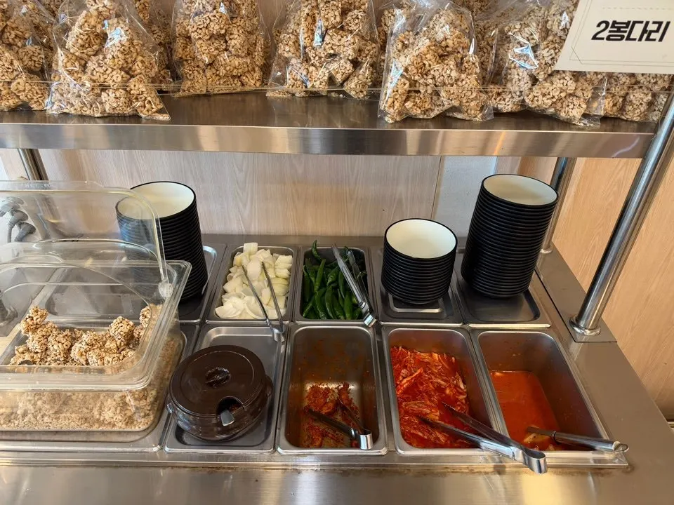 Self-serve bar with puffed barley crackers and kimchi at Hoegi Wang Galbitang