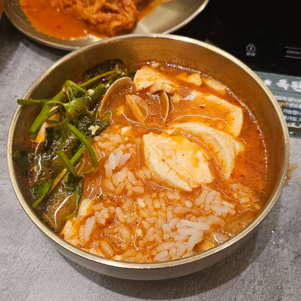 A spoonful of sundubu and clams lifted from the pot