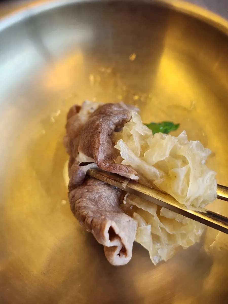 Cooked shabu beef and vegetables lifted out of the pot