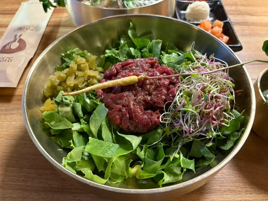 Special soy-sauce yukhoe bibimbap topped with a whole stalk of ginseng