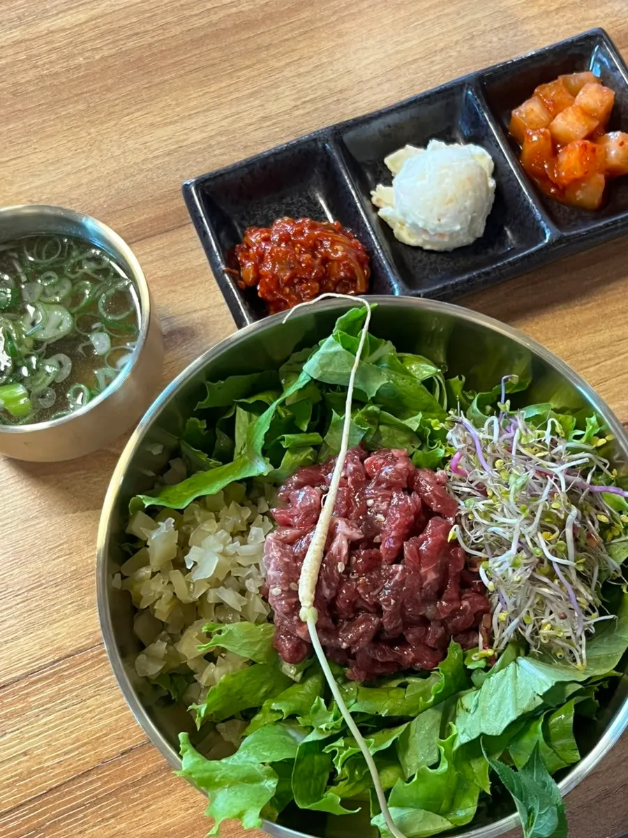 Full table setting of beef soy sauce yukhoe bibimbap with gomtang and side dishes