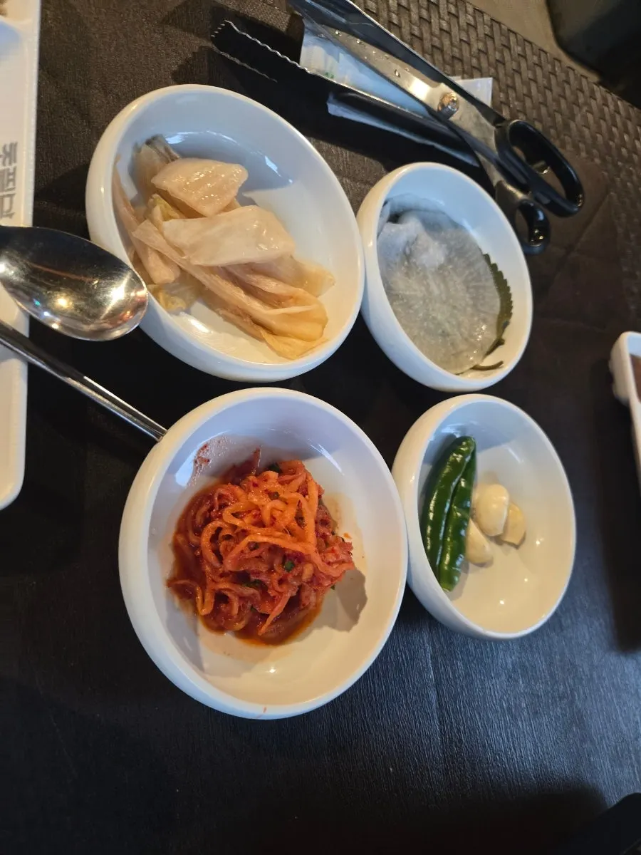 Plate of banchan including pickled radish, perilla leaves, and scallion salad