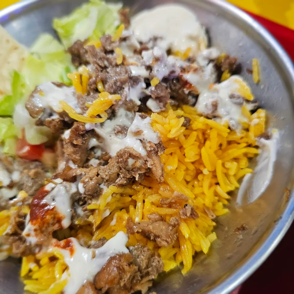 Rice drizzled with white sauce alongside lettuce and tomato
