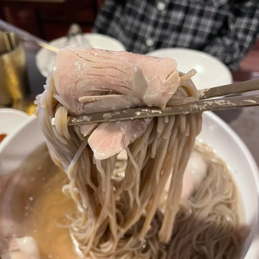 Naengmyeon noodles lifted with chopsticks