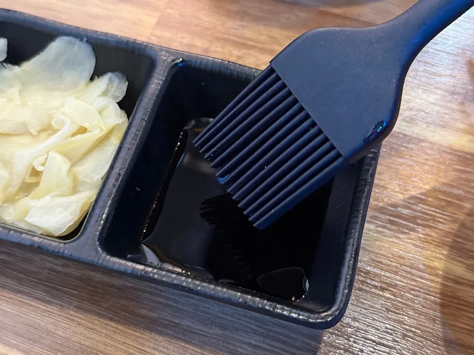 Untando salsa de soja con pincel sobre nigiri de cola larga