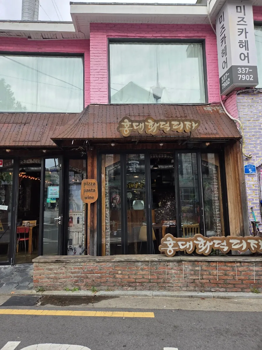 Exterior of Hongdae Hwadeok Pizza with log wood and red brick