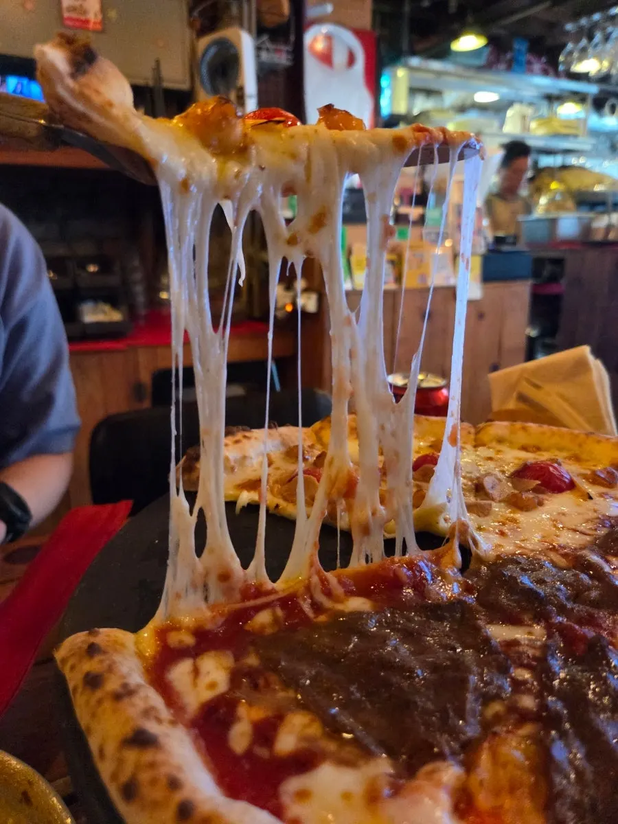 A slice of wood-fired pizza with cheese stretching
