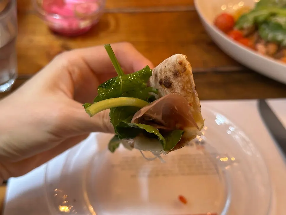 A rolled slice of Rucola Prosciutto pizza held by hand