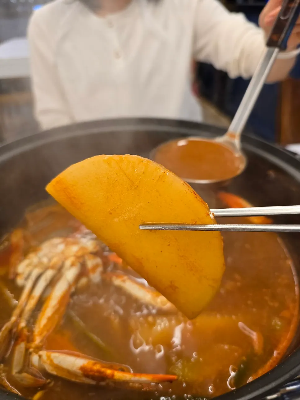 Ladle scooping crab soup broth with radish