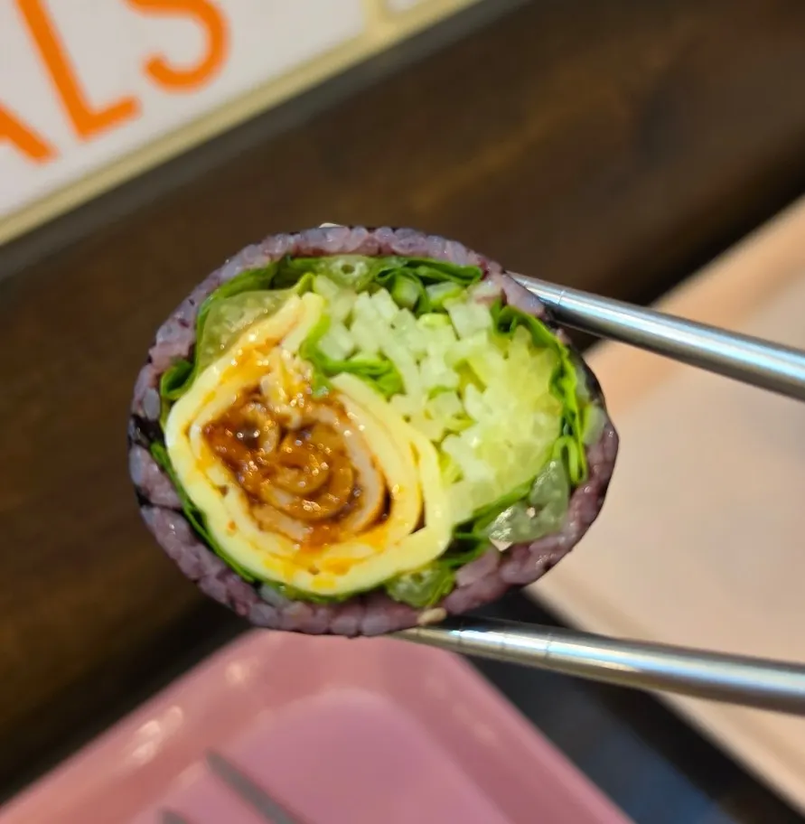 A piece of spam gimbap picked up with chopsticks