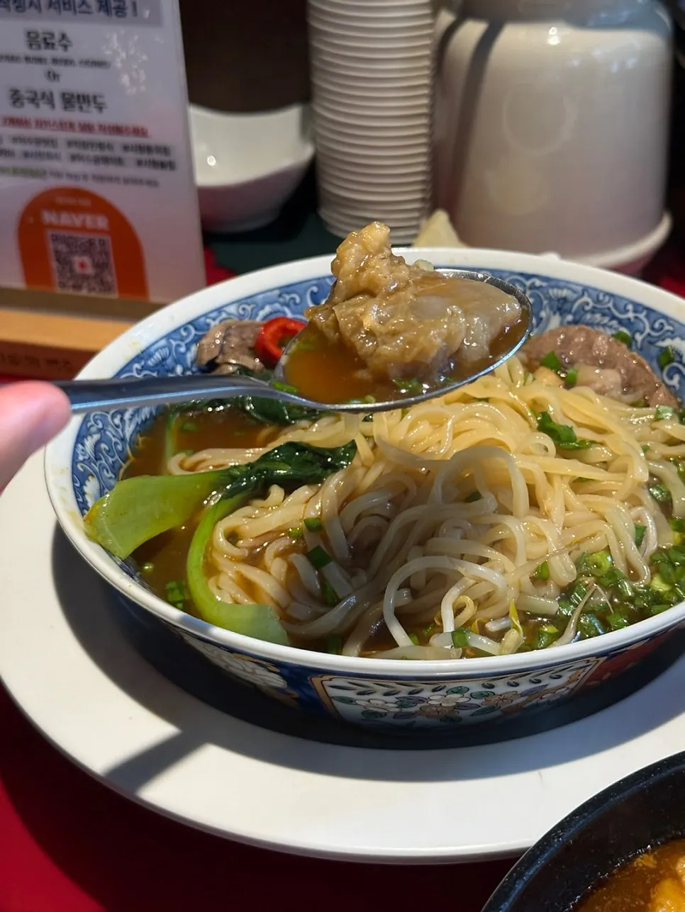A bowl of Huhugwan's beef noodle soup topped with bok choy