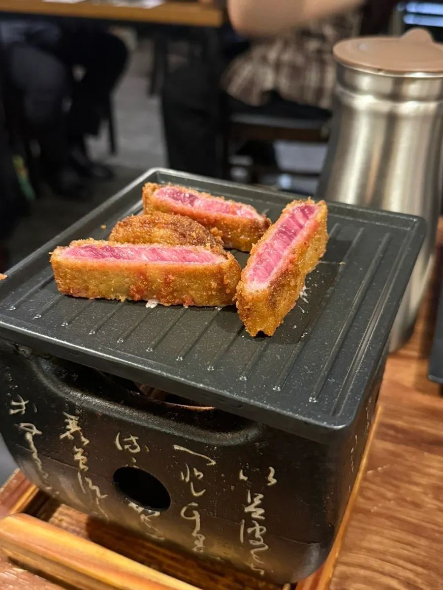 A piece of gyukatsu being grilled on a personal tabletop brazier
