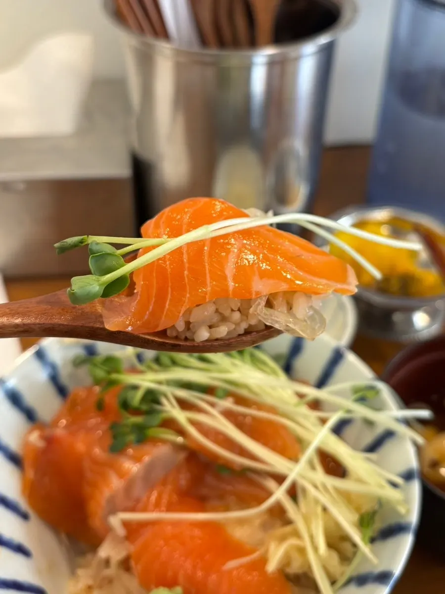 A piece of salmon topped with wasabi and radish sprouts