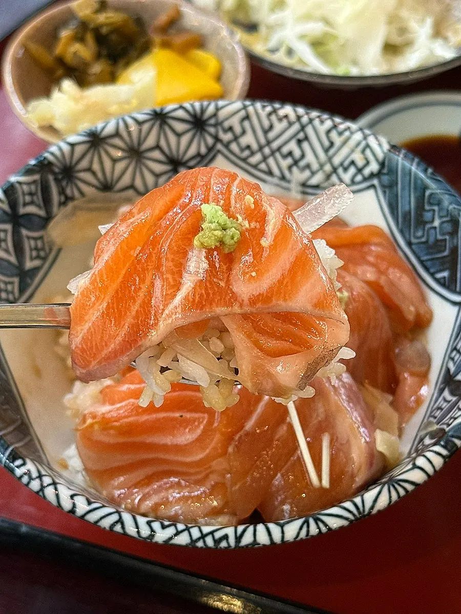 A bite of the salmon bowl topped with onion and wasabi
