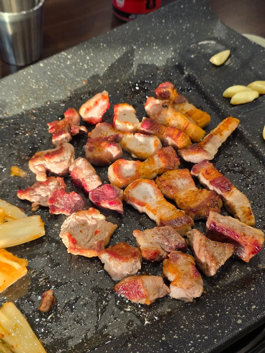 Pork belly grilling on the tabletop grill with roasted garlic and kimchi