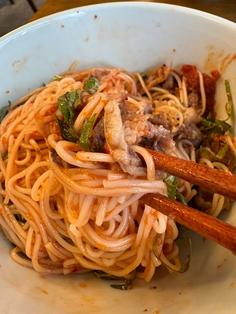 A bite of herring roe bibim noodles lifted with chopsticks