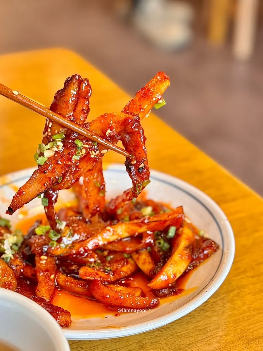 A bite-sized piece of grilled deodeok and mushrooms picked up with chopsticks