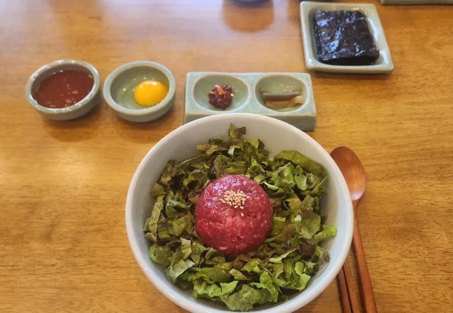 Full table setting with yukhoe bibimbap, side dishes, and dried gim