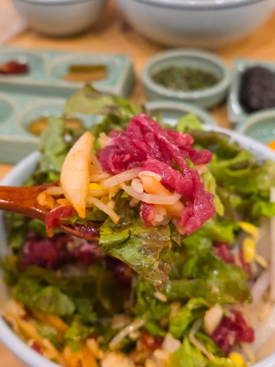 A spoonful of yukhoe bibimbap showing pear and bean sprouts