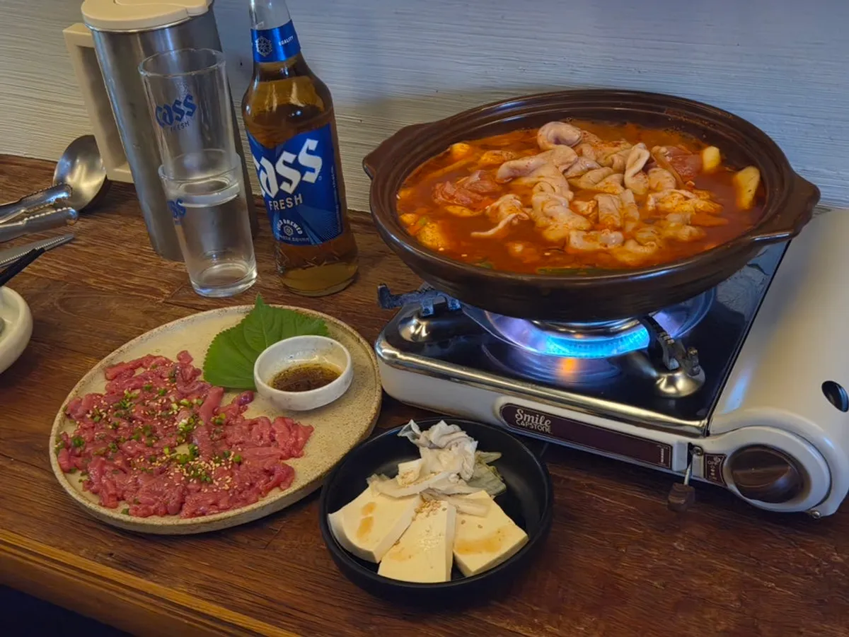 A table at Hyehwahwa set with gopdori-tang, yukhoe, and beer
