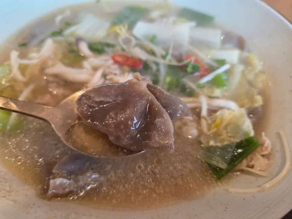 Lifting up a bite of Hyeondae Memil's soy sauce mak guksu noodles