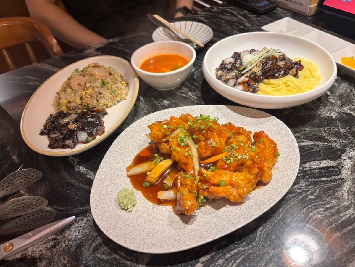 Table spread with ganjjajang, fried rice, sweet and sour pork, and eggplant mandu