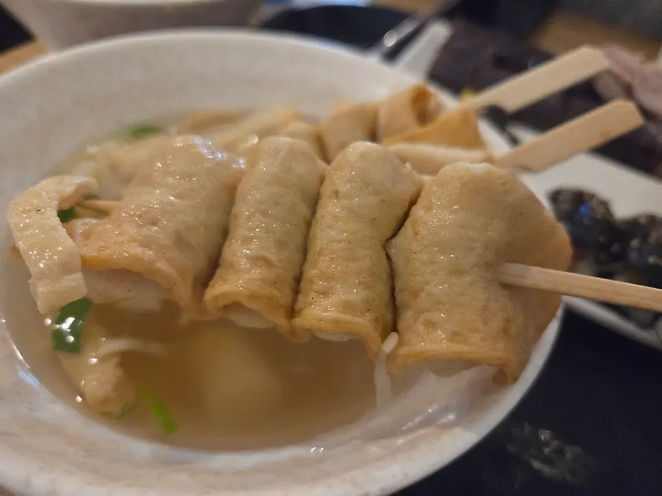 Three fish cake skewers and fish cake broth on a plate