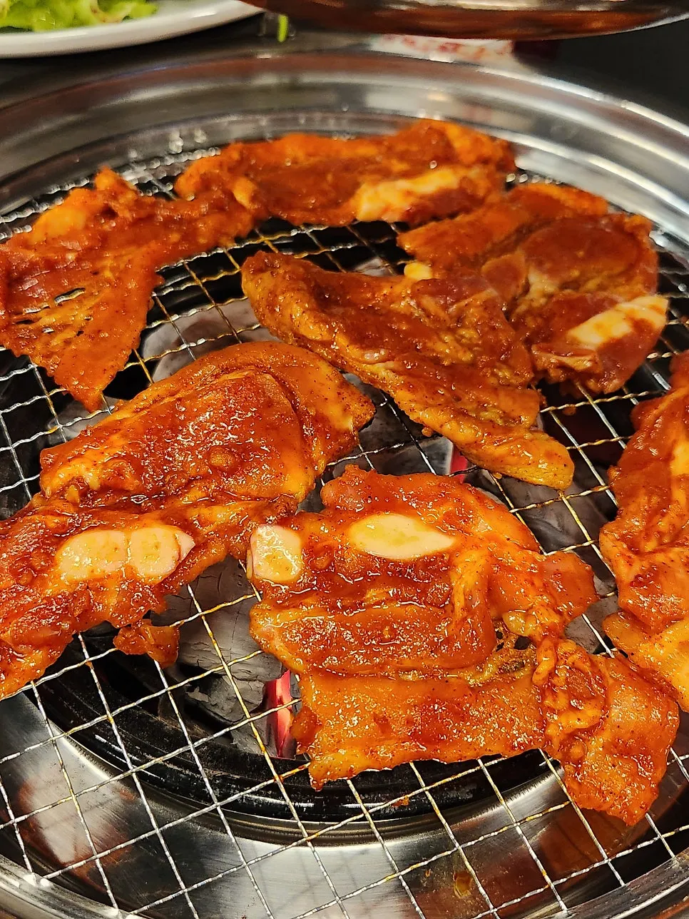 Seasoned pork belly grilling on a charcoal plate