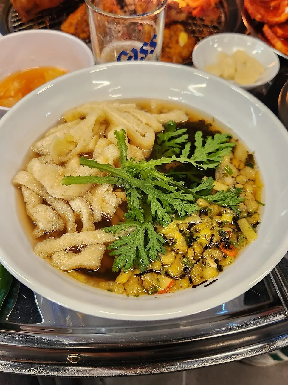 A bowl of udon topped with crown daisy leaves