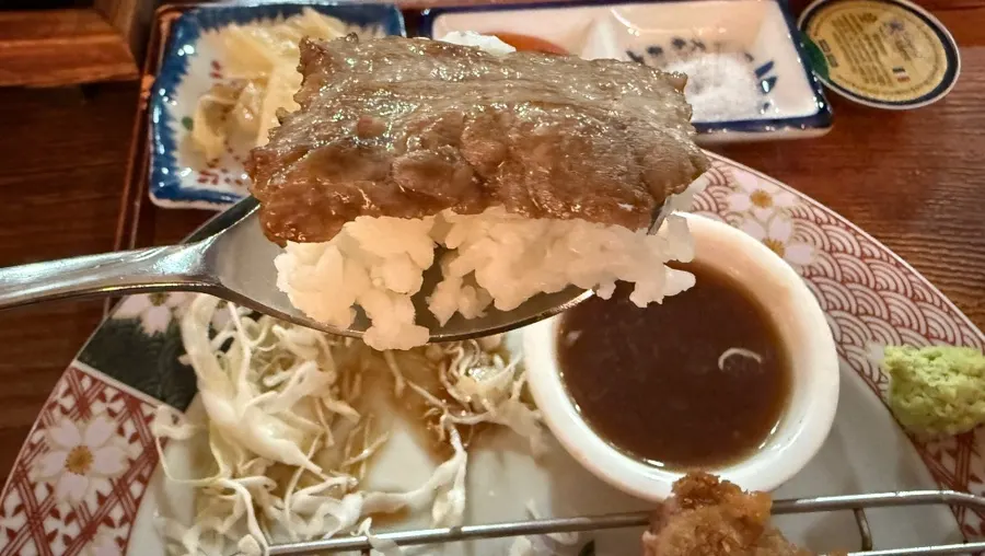 A piece of steki dipped in steak sauce with wasabi on top