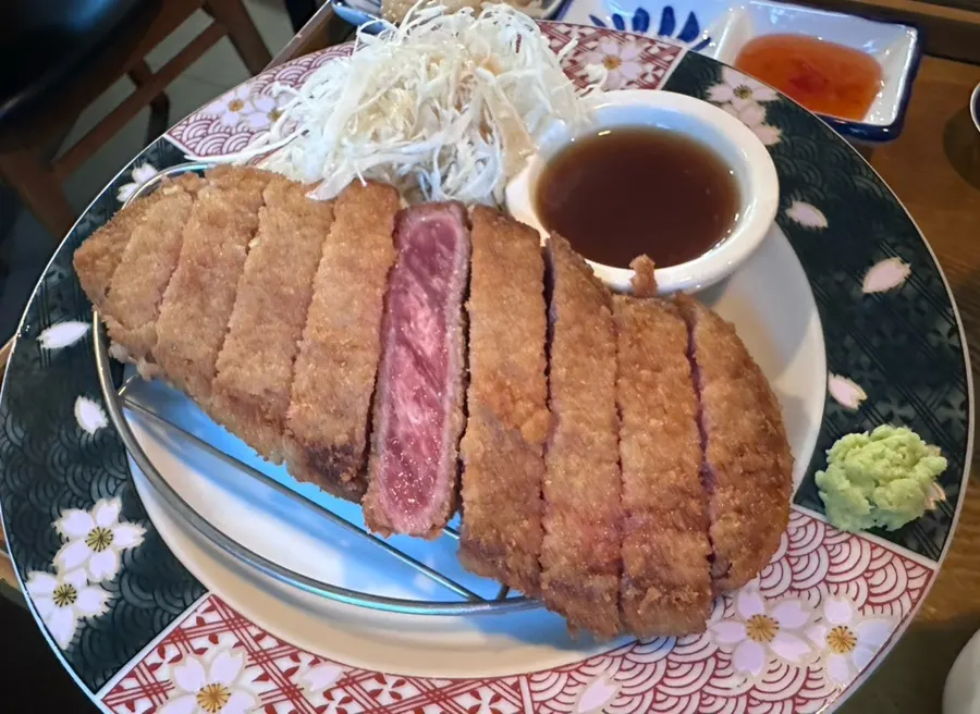 Sekeping gyukatsu sedang digoreng atas dulang panas