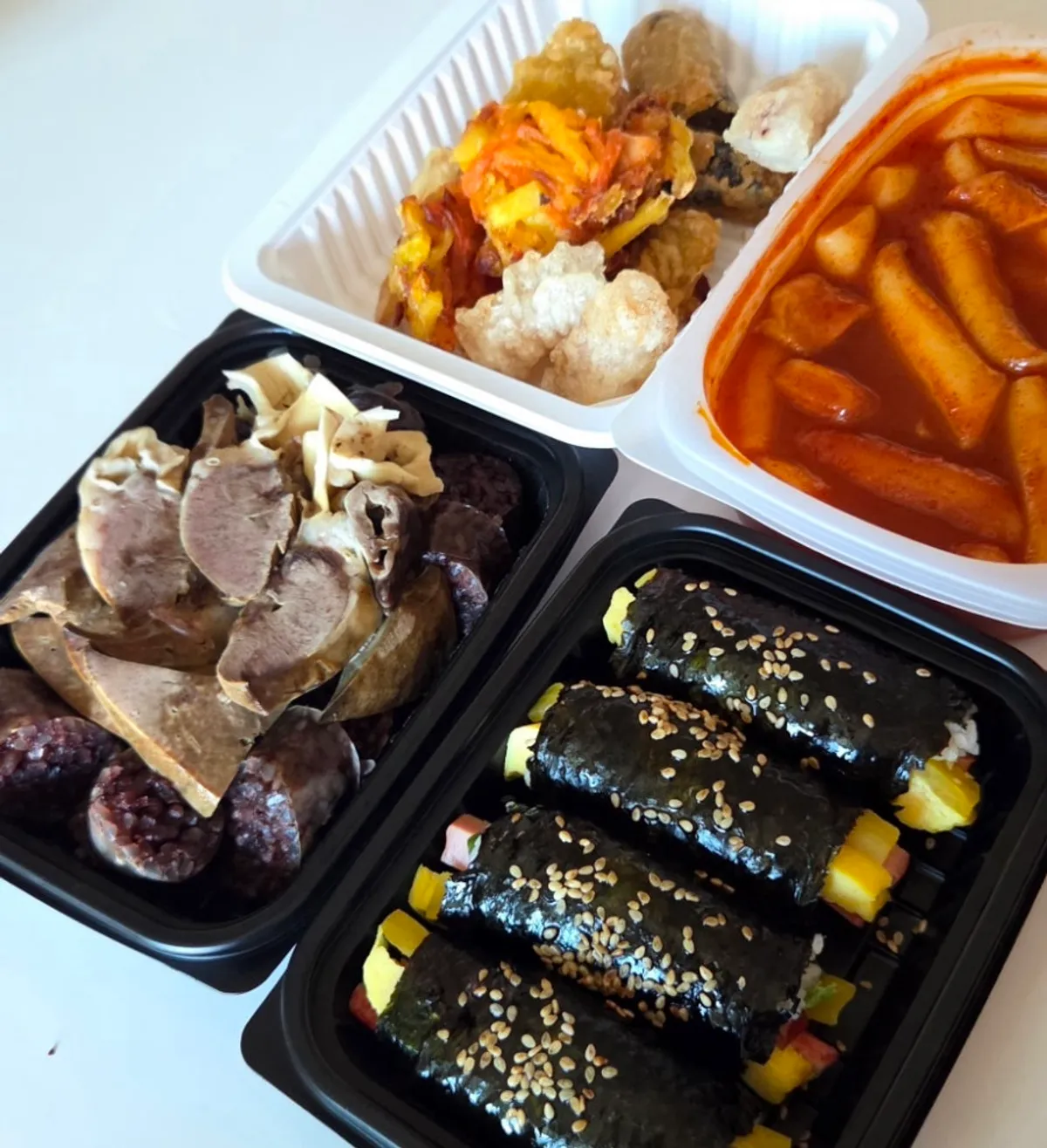 Hyeonseoni Set of tteokbokki, sundae, fried snacks, and gimbap laid out on a table