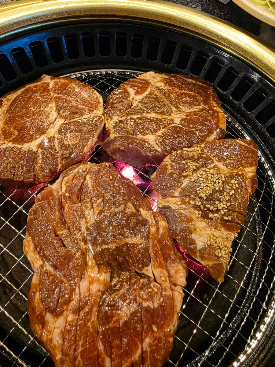Staff member grilling thick cuts of marinated pork galbi