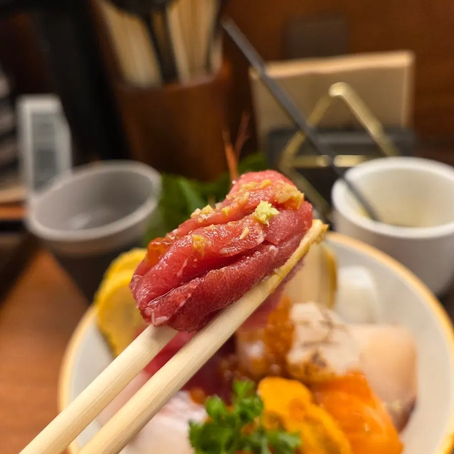 A single piece of tuna sashimi lifted with chopsticks