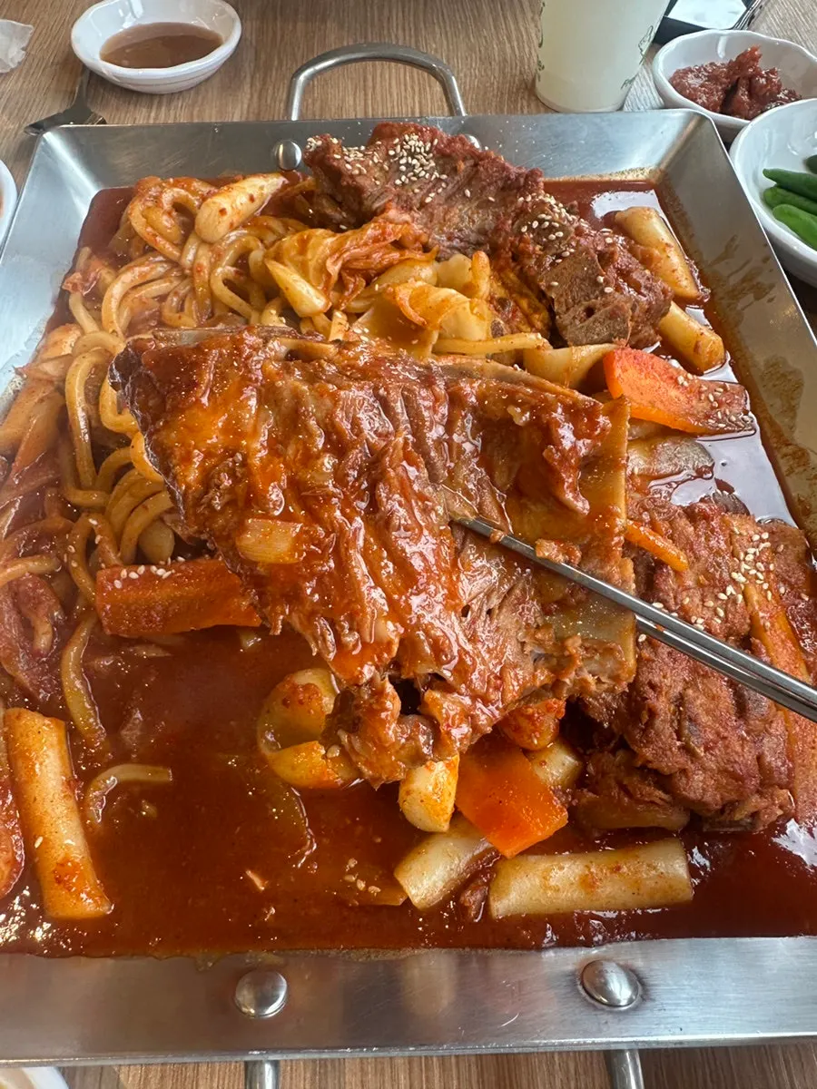 A full platter of small spicy bone stew with udon noodles, rice cake, and sujebi