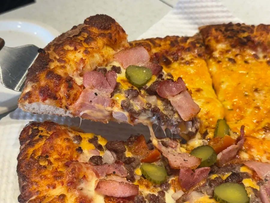A heavily topped slice of Melting Cheeseburger pizza