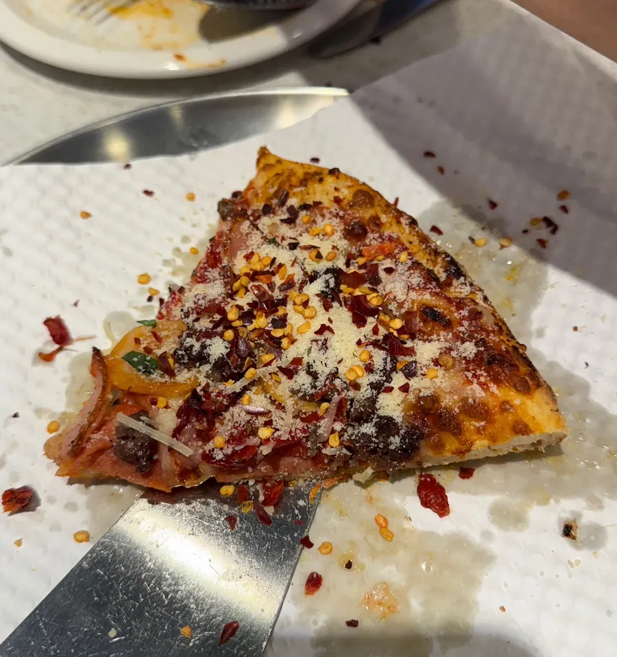 A slice of pizza served with pickles and house sauce