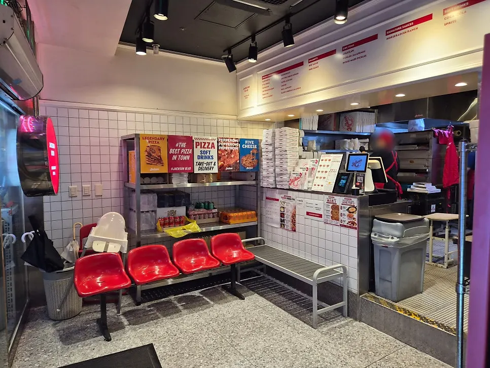 Seating with red chairs and an English pizza poster on the wall