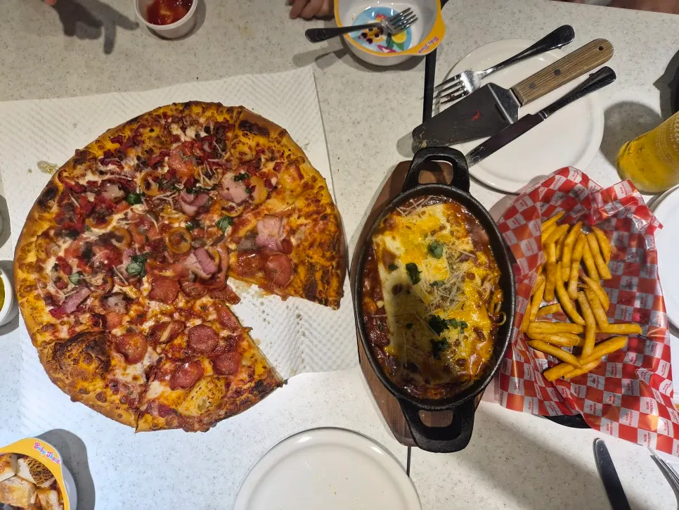 A table spread of pizza, pasta, and French fries