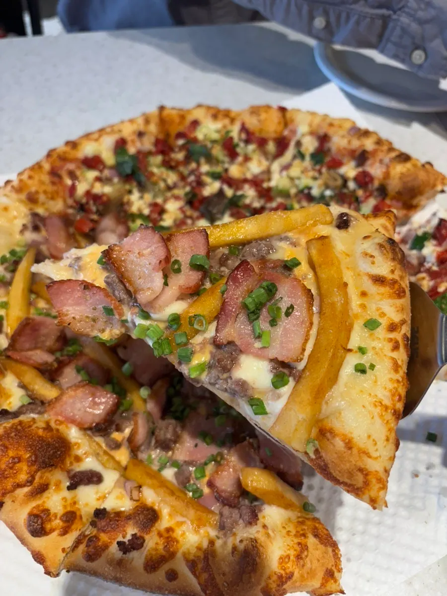A slice of Greekology pizza loaded with vegetable toppings