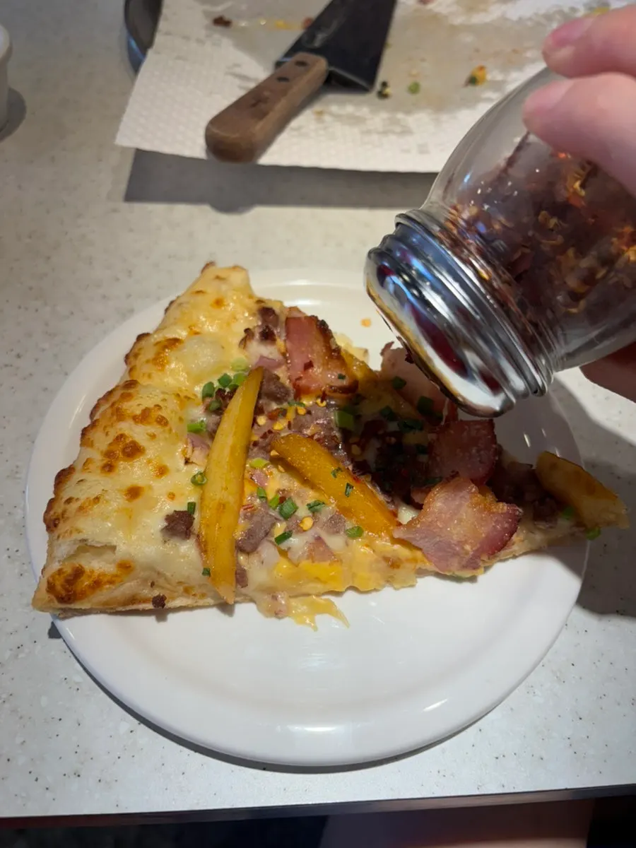 A slice of pizza sprinkled with red pepper flakes